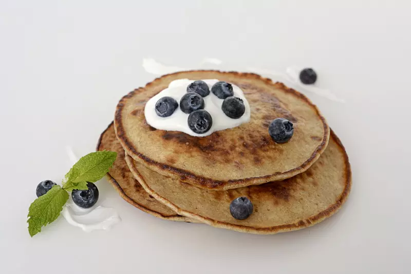a stack of three homemade pancakes, topped with a dollop of Greek yogurt and fresh blueberries