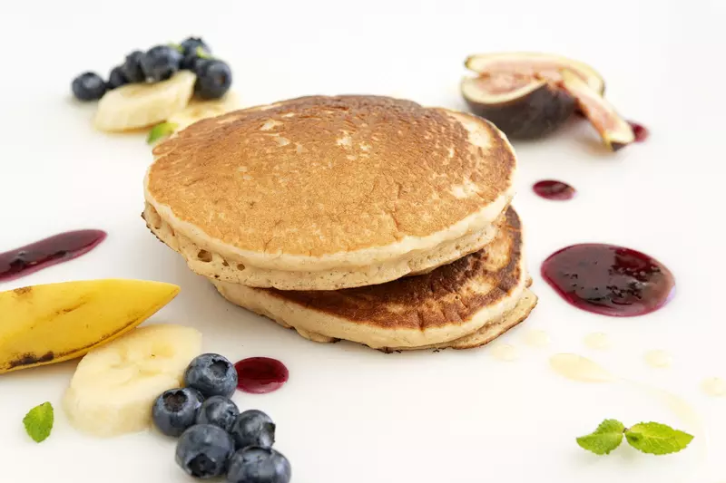a short stack of pancakes, surrounded by fresh blueberries, banana slices and other fruit