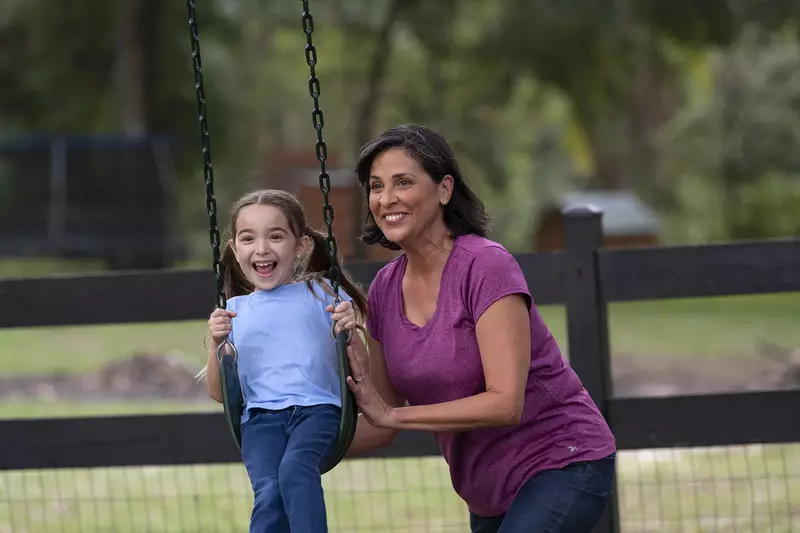 Middle aged woman pushing a little girl on a swing at the park