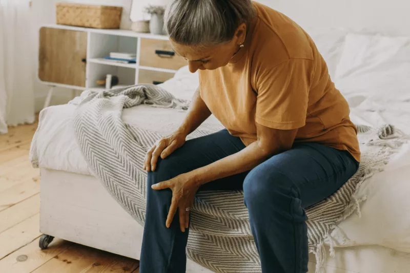 Woman sitting down at home and holding leg in pain.