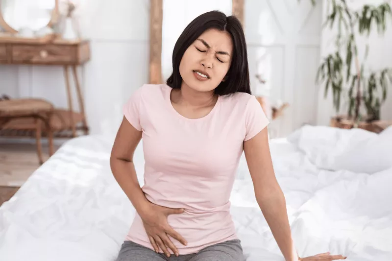 Woman sitting and holding lower abdomen in pain.