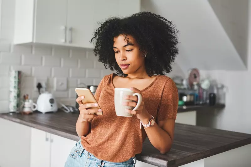 Woman during her morning routine: a cup of coffee while checking her phone.