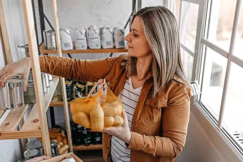 A woman holding a sack of potatoes and a can in a pantry.