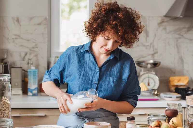 Woman pouring milk into a bowl while in a kitchen at home.