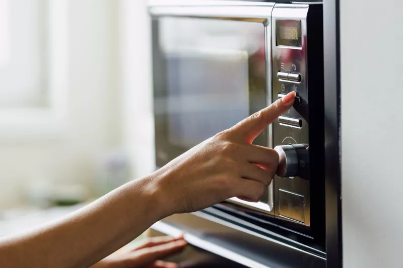 A woman pressing a button of a microwave.