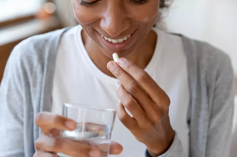 Woman taking a probiotic with a glass of water.