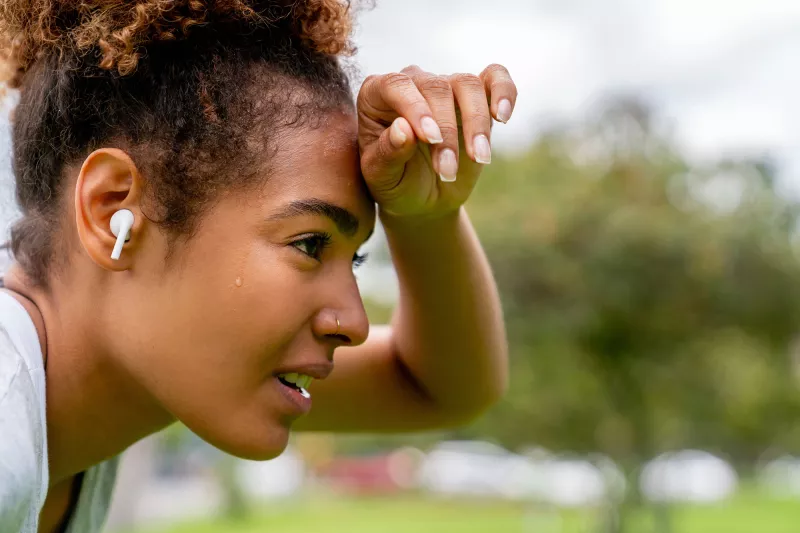 A woman wipes her brow while taking a break from exercising outdoors.