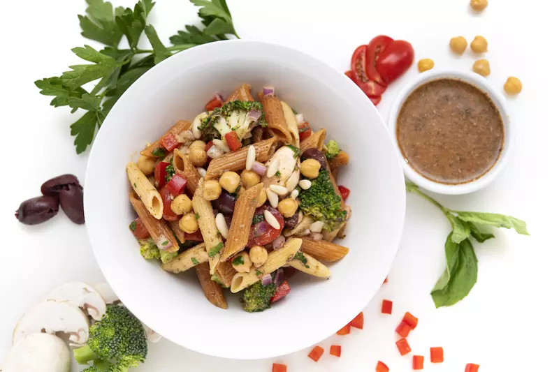 Bowl of pasta salad with brown sauce and leaf garnishes on the side