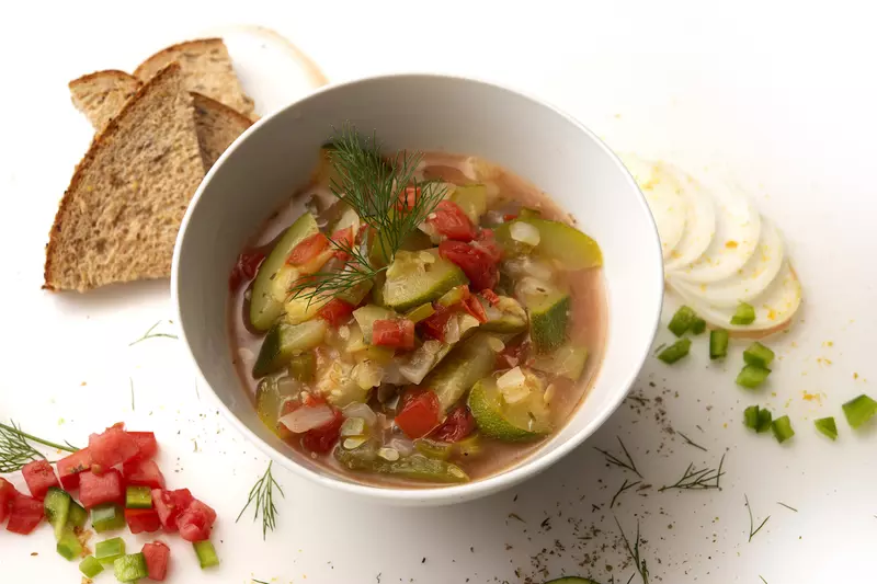 Bowl of zucchini creole with toast and onion, pepper, and herb garnishes