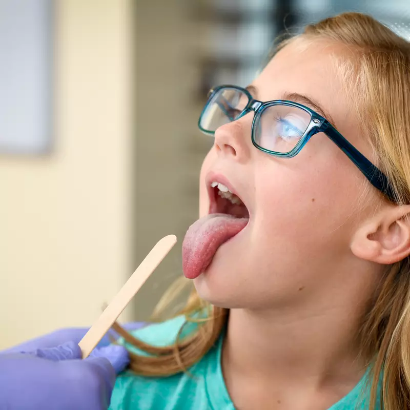 A Centra Care Patient Sticks Out Her Tongue as a Tongue Depressor Comes Into View 