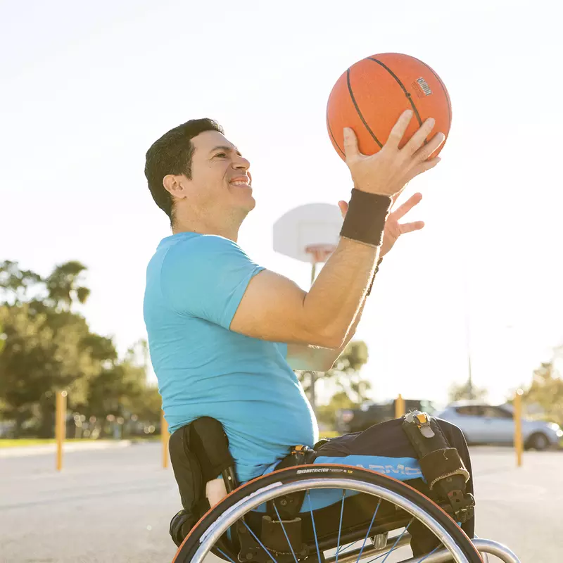 A Caucasian man in a wheelchair practices tricks with a basketball.