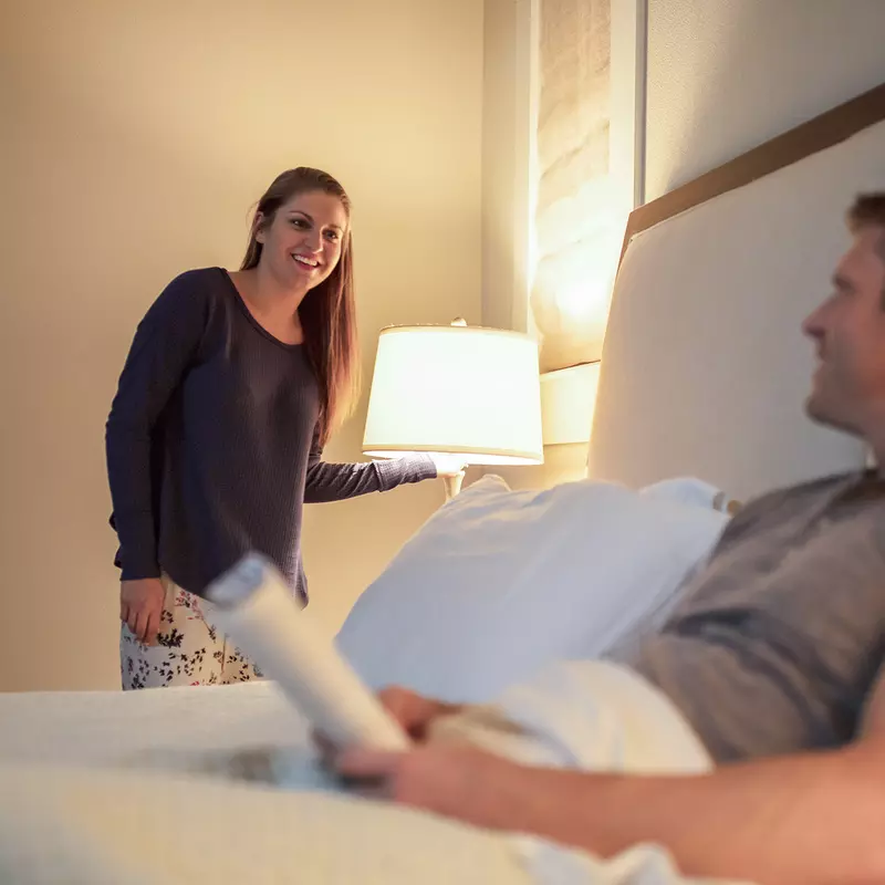 A young Caucasian couple smile at each other before turning off the lights for bed.