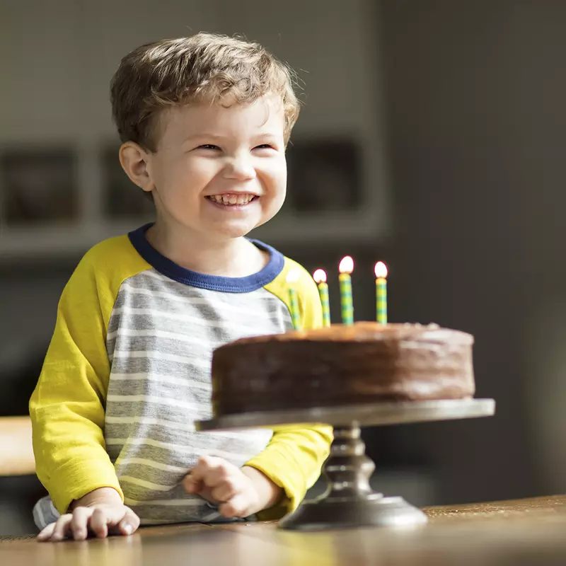 A young boy smiles before blowing out the four candles on his chocolate birthday cake.