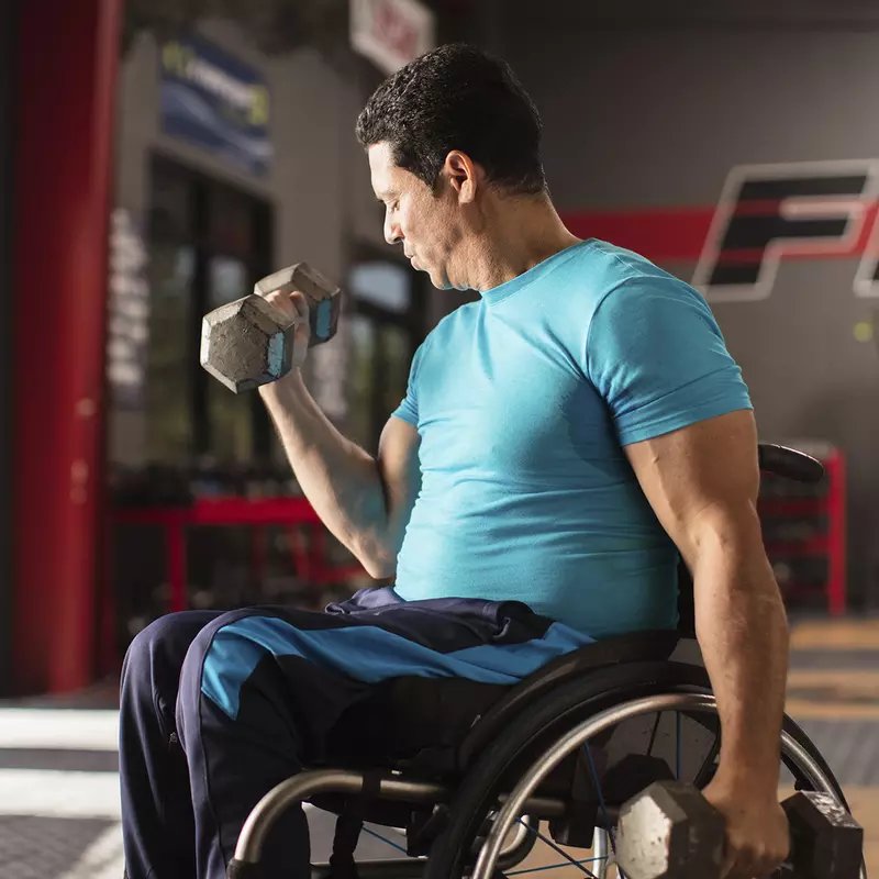 A man in a wheelchair lifts free weights at the gym. 