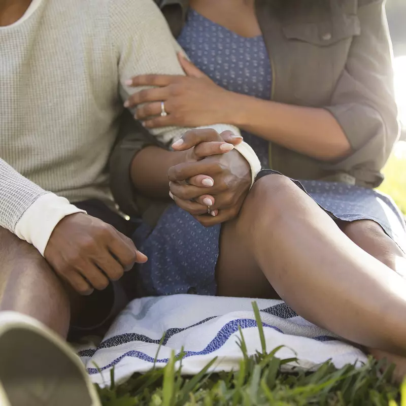 A young African American couple holds hands during an outdoor picnic.