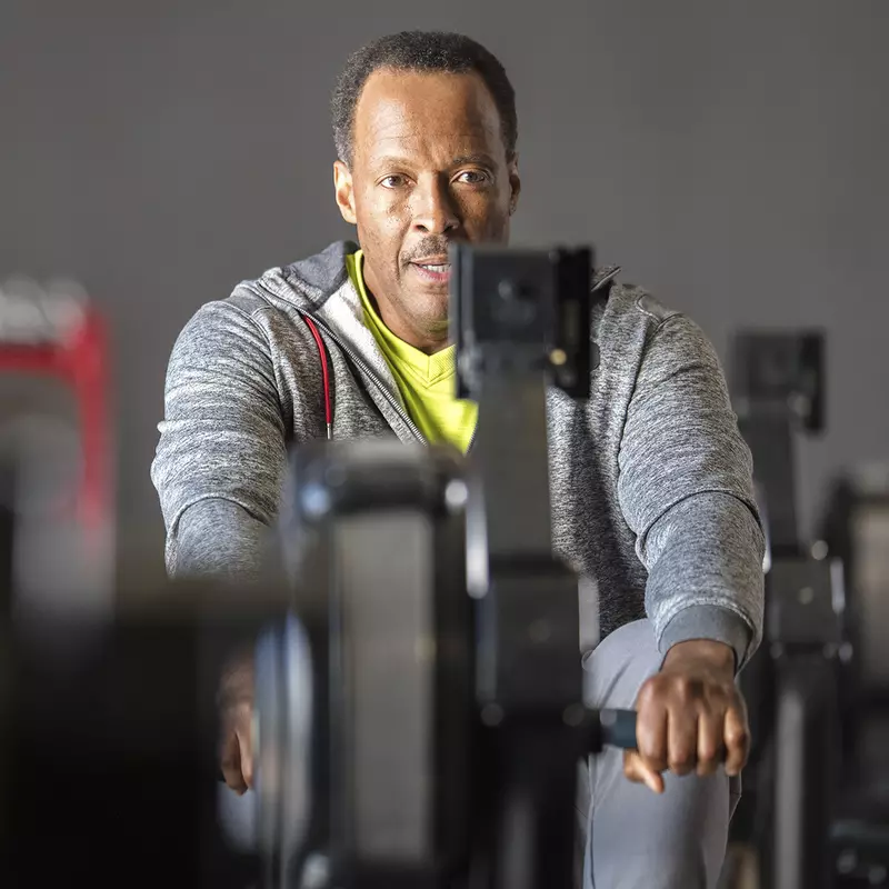 An older African American man works out on a rowing machine at the gym.