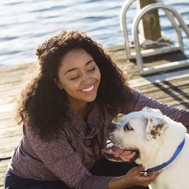 A young African American women plays with her dog on a dock by the lake.