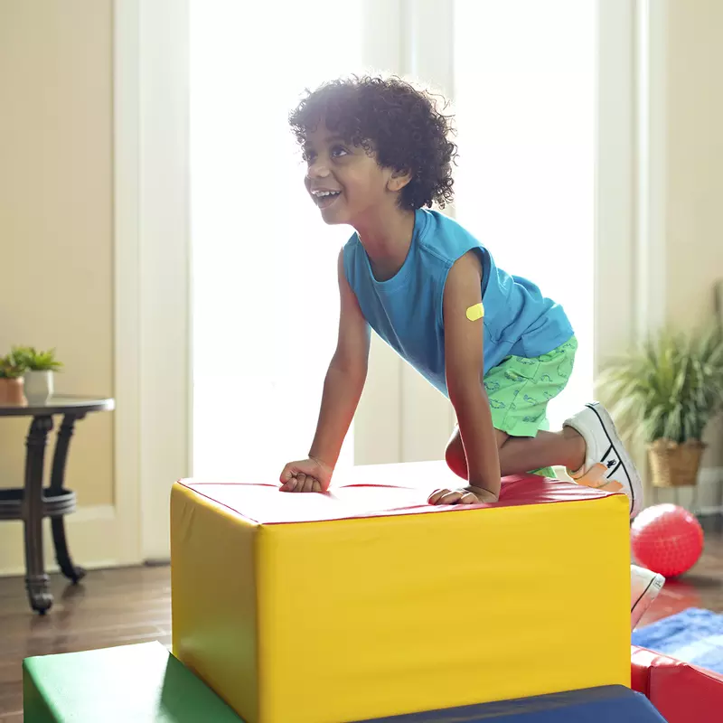 A young African American boy plays on cushioned toy blocks at home.