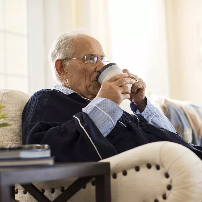 An elderly Caucasian man sips coffee on a couch.