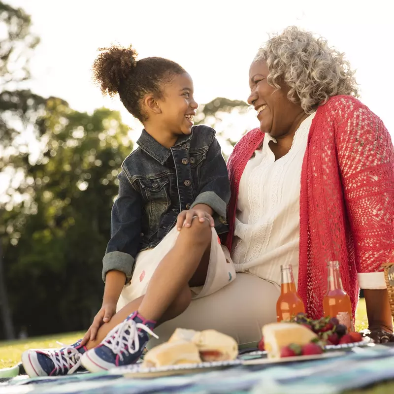 An African American granddaughter and grandmother sit outside for an evening picnic.