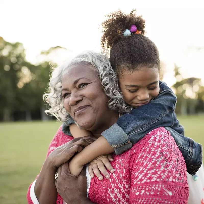 An African American granddaughter embraces her grandmother around the neck.