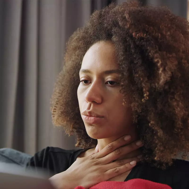 A woman touching her throat and showing discomfort