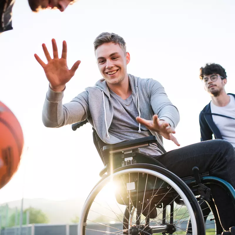 Older teens playing basketball one of which is in a wheelchair 