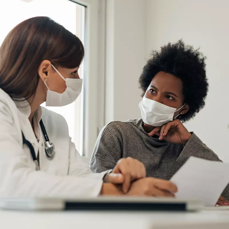 Doctor speaking to her patient about her treatment options while wearing masks in practice office