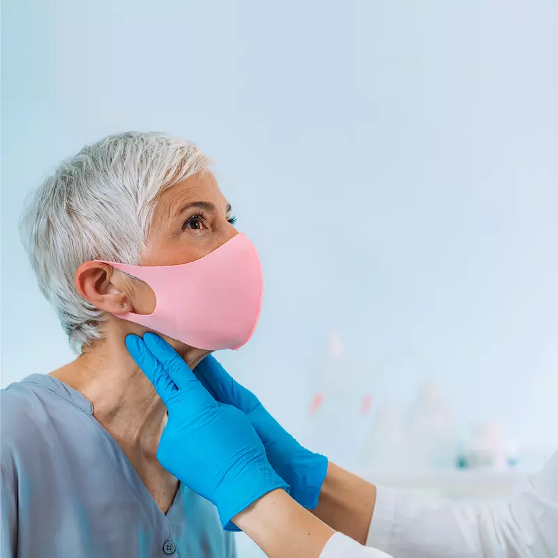 A Doctor examines a patient's neck while they both wear face coverings