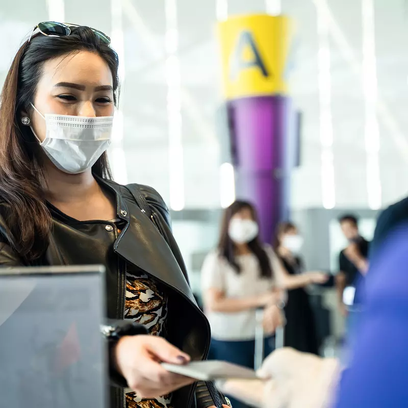 Lady checking in for a flight at an airline counter wearing a covid mask