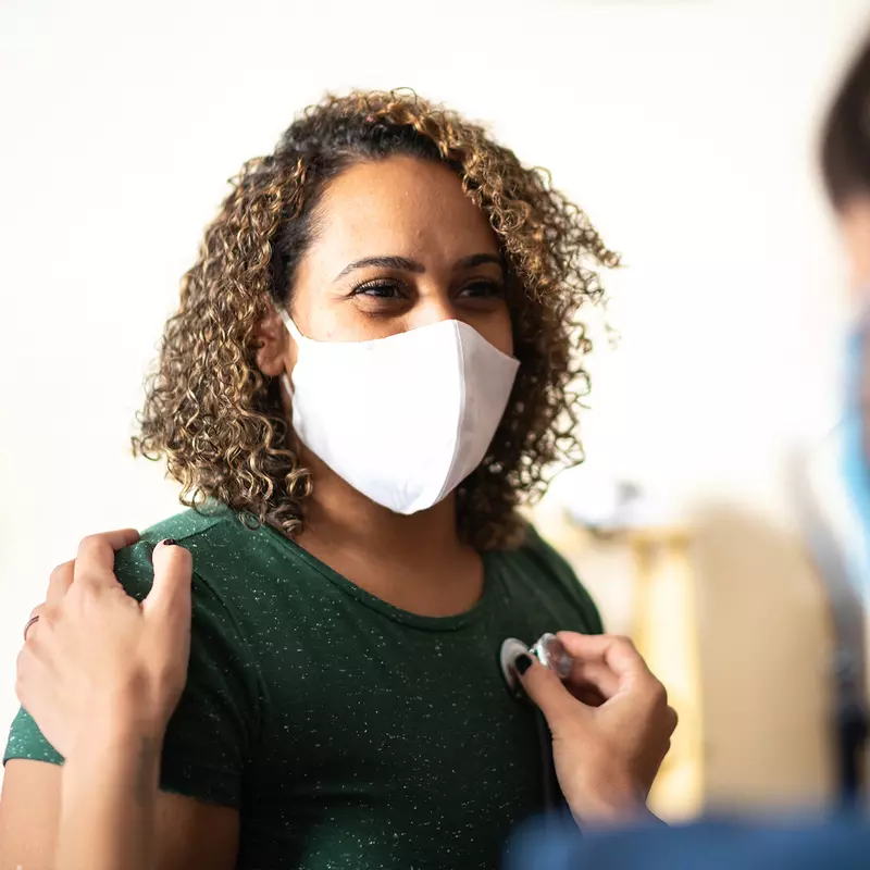 A Woman Wearing a Face Mask has her Vitals Taken by a Care Provider