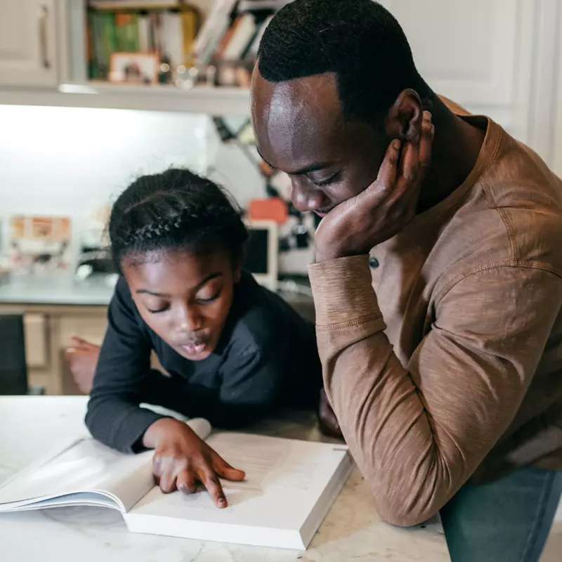 A Father Helps His Daughter Complete Her Homework in the Kitchen of Their Home.