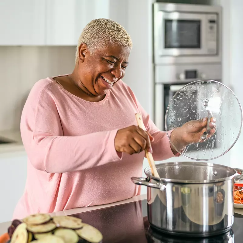 A Woman Gleefully Mixes a Large Pot on a Stove Top in a Modern Kitchen.