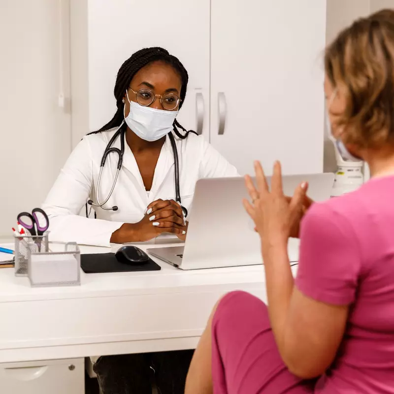 A Doctor Wearing a Face Mask in Her Office Speaks with a Patient about Her Care.