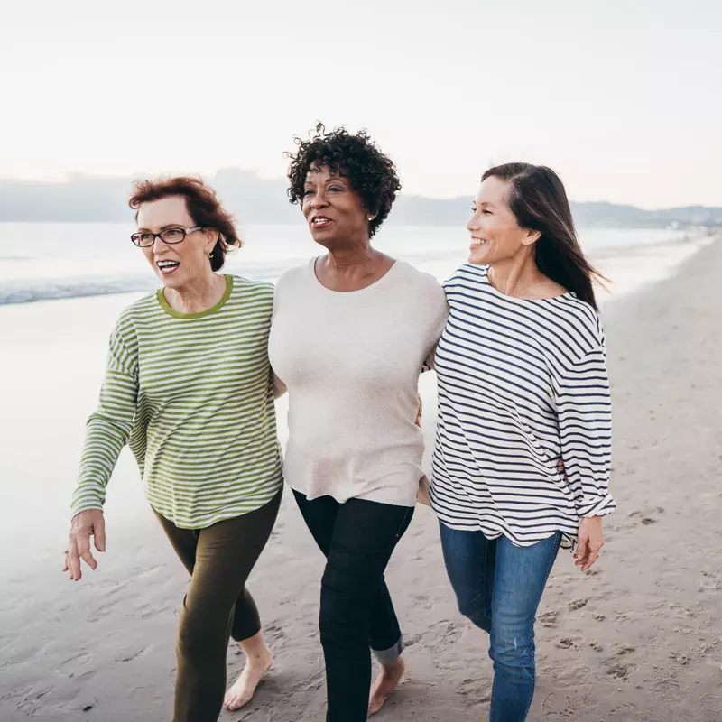 Three ladies walk arm in arm on the beach