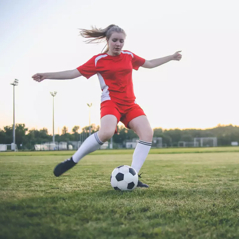 A Teenage Girl Soccer Player Kicks a Ball on the Pitch.