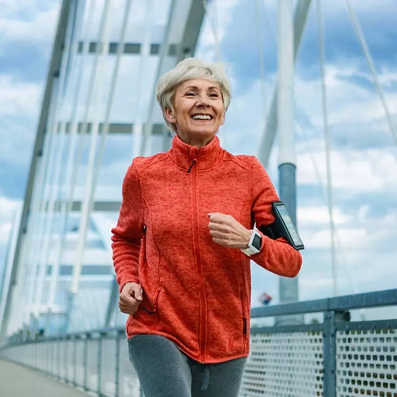 A Senior Woman Jogs Across a Bridge While Listening to Music