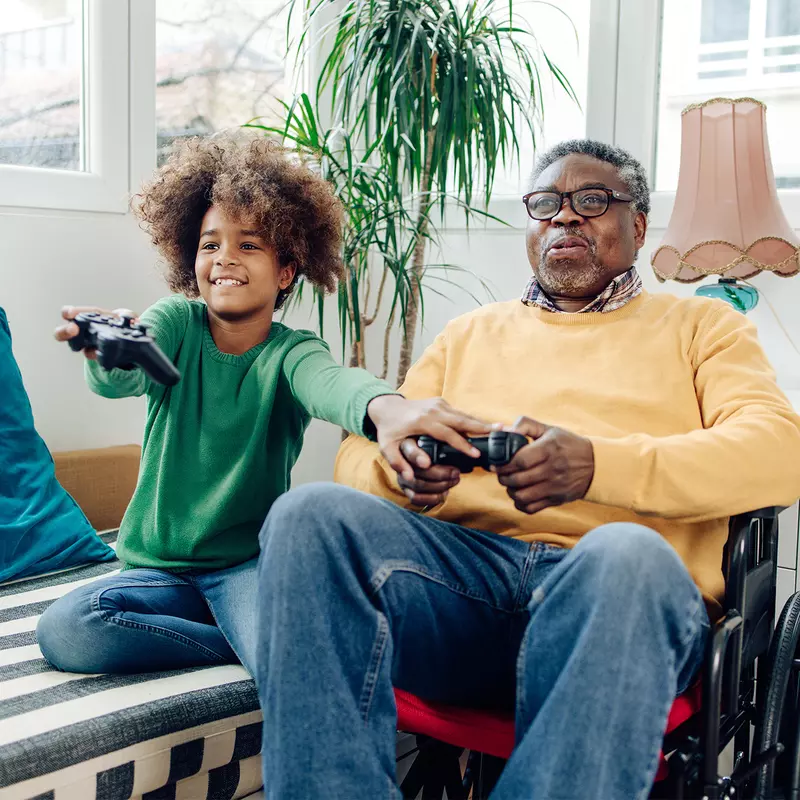 A Grandfather in a Wheelchair Plays Video Games with His Grandson who is Teaching Him How To Play.