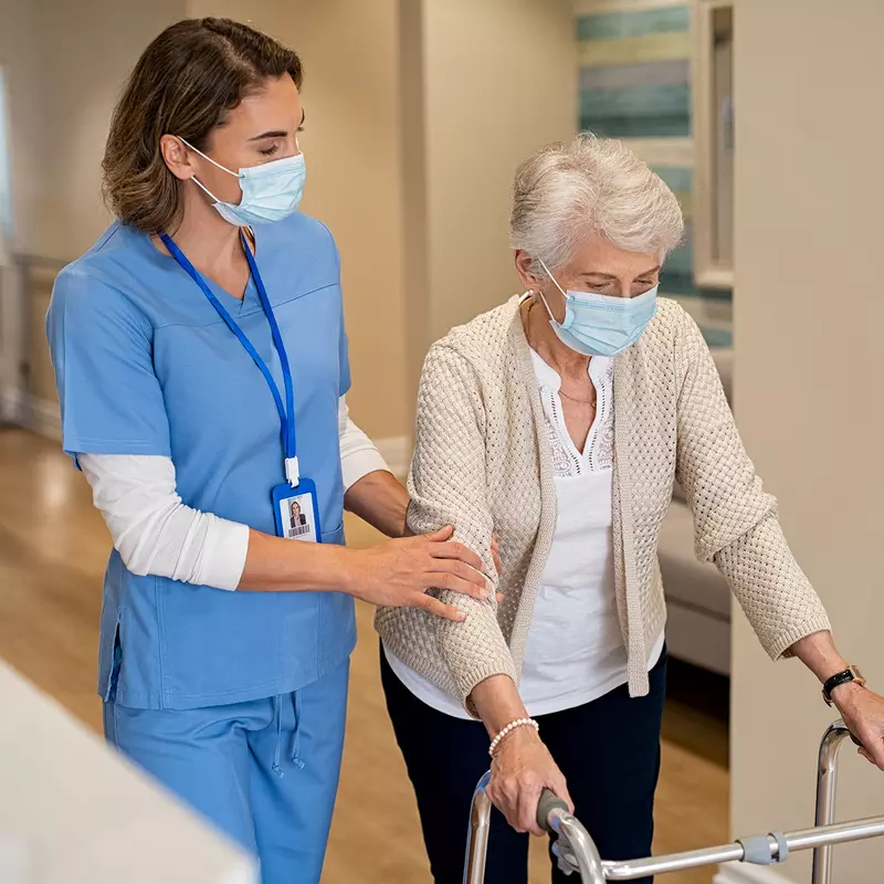 A Nurse Helps an Elderly Patient Navigate the Hallway of the Facility.