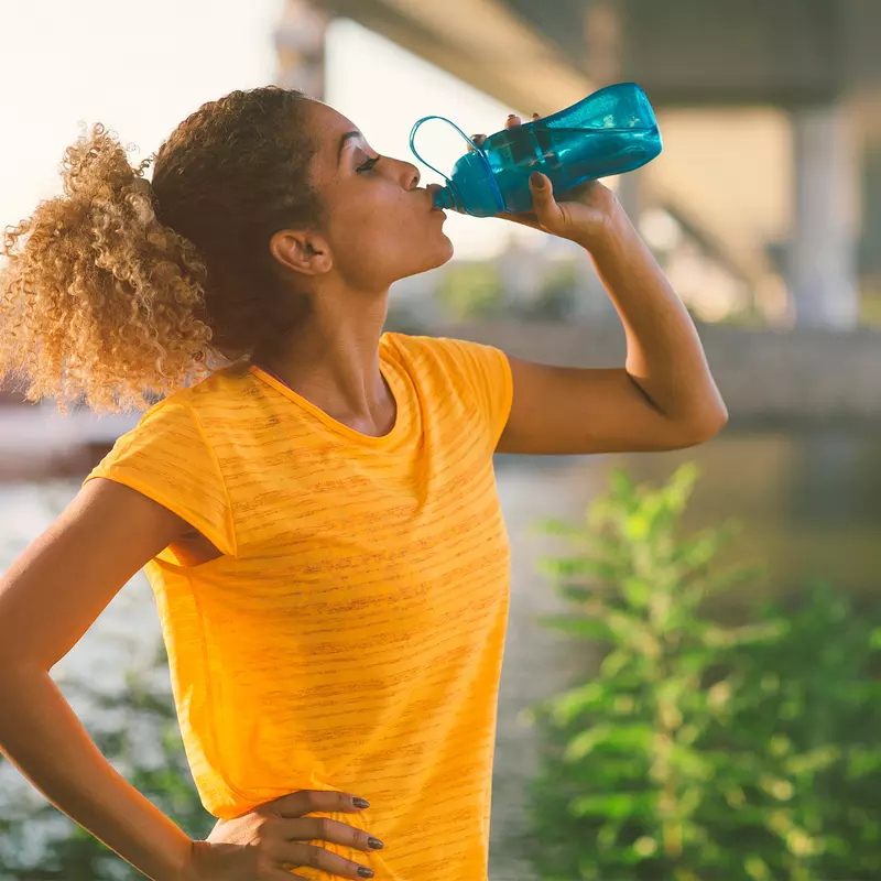 A Woman Takes a Water Break by a Waterfront During a Run
