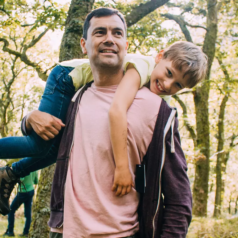 A Man Carrying His Son in a Playful Manner Over His Shoulders Through the Woods.