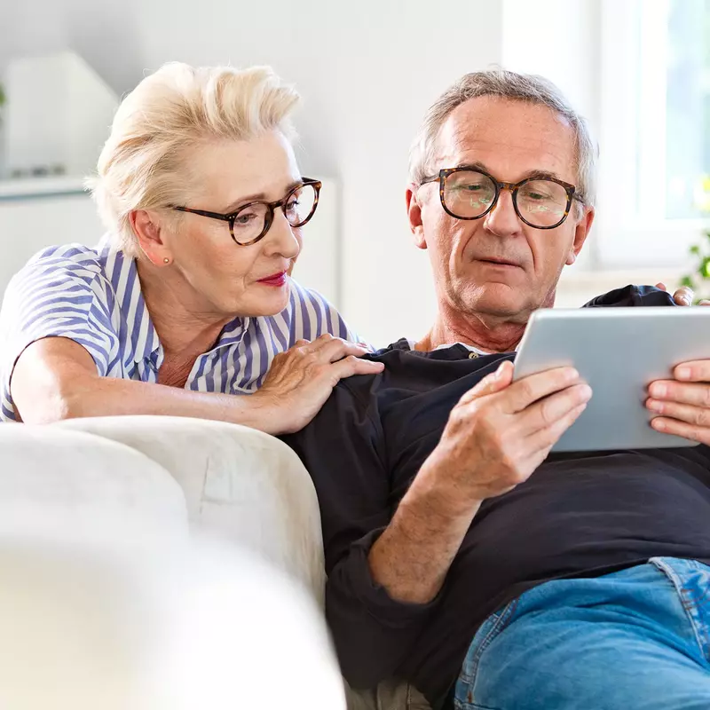 A Senior Couple Looks at a Tablet Together in Their Living Room.