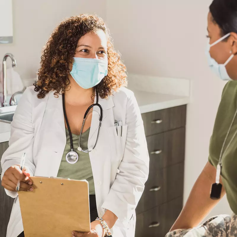 A Doctor Speaks to Her Patient in an Exam Room While Wearing a Face Mask.