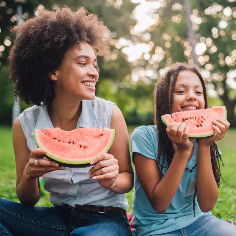 A Mother and Daughter Sit at a Picnic Enjoying Fruit