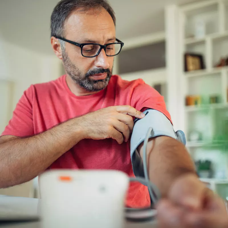 A Man Puts a Blood Pressure Cuff on His Arm in His Home.