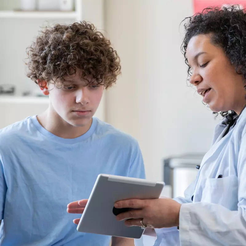 A Physician Goes Over a Teenager's Chart on a Tablet