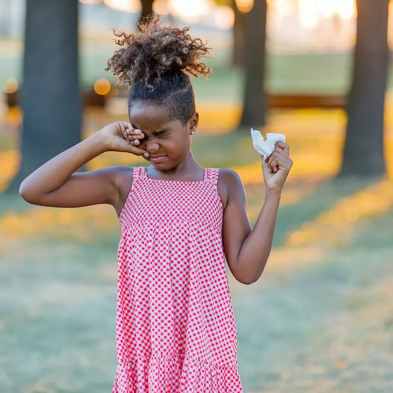 A Child Rubs Her Eye While Walking Through a Park
