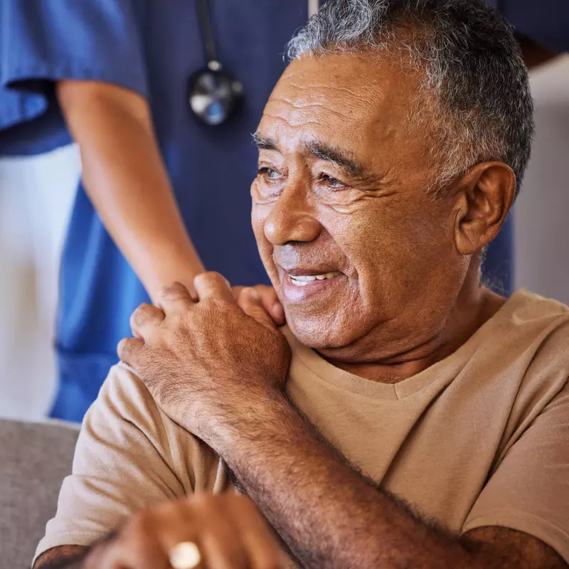 A Senior Man Smiles as a Nurse Puts Her Hand on His Shoulder for Comfort.