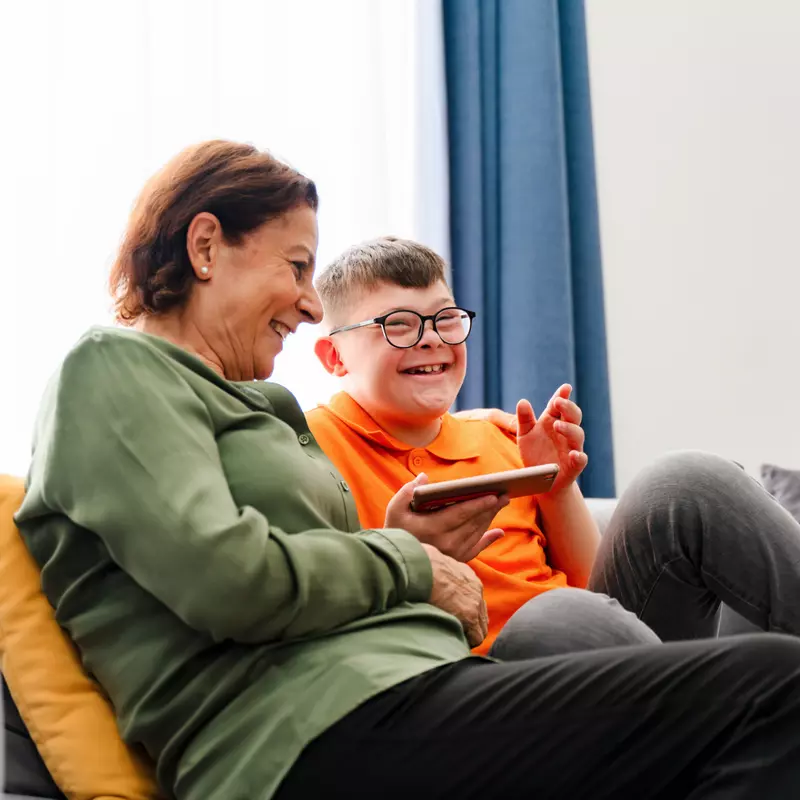 A Child with Down Syndrome Smiles While he and his Mother Look at Content on an iPad