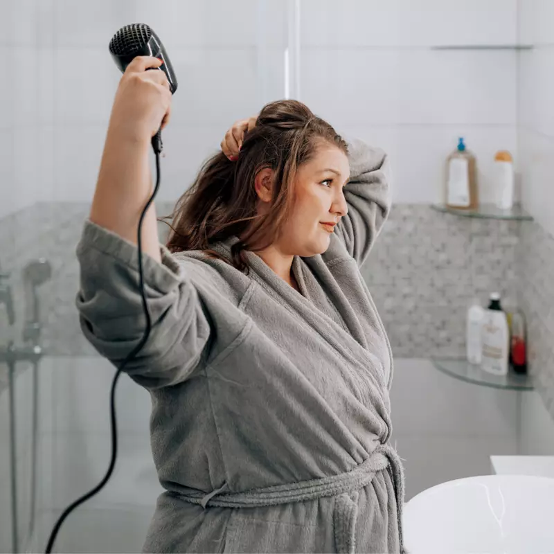 A Woman Blow Dries Her Hair in the Bathroom Mirror